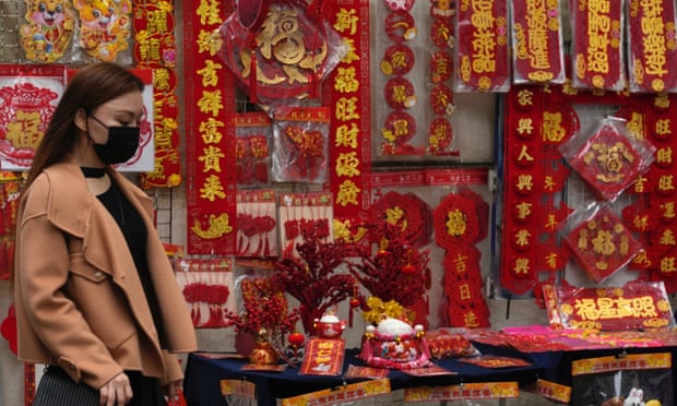 Một người phụ nữ đi qua những tờ tiền có chứa thư pháp và đồ trang trí Tết của Trung Quốc được trưng bày trên một con phố để chào mừng Tết Nguyên đán vào ngày 14 tháng Giêng. Ảnh: Kin Cheung / AP
