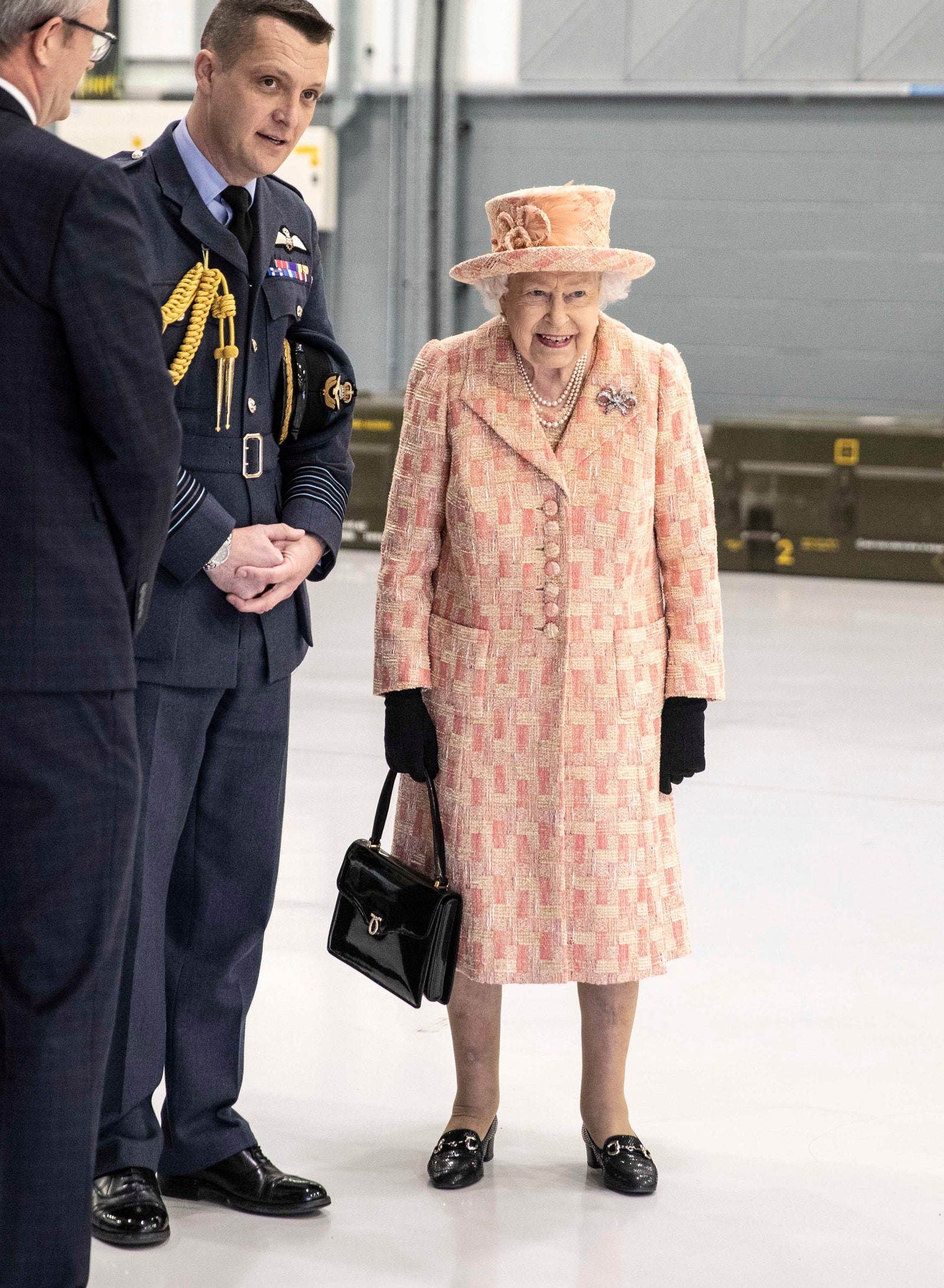 Nữ hoàng đã chọn một bộ quần áo dài màu hồng đào nhạt với chiếc túi xách Launer đặc trưng của mình khi đến thăm một căn cứ Không quân Hoàng gia ở King's Lynn.