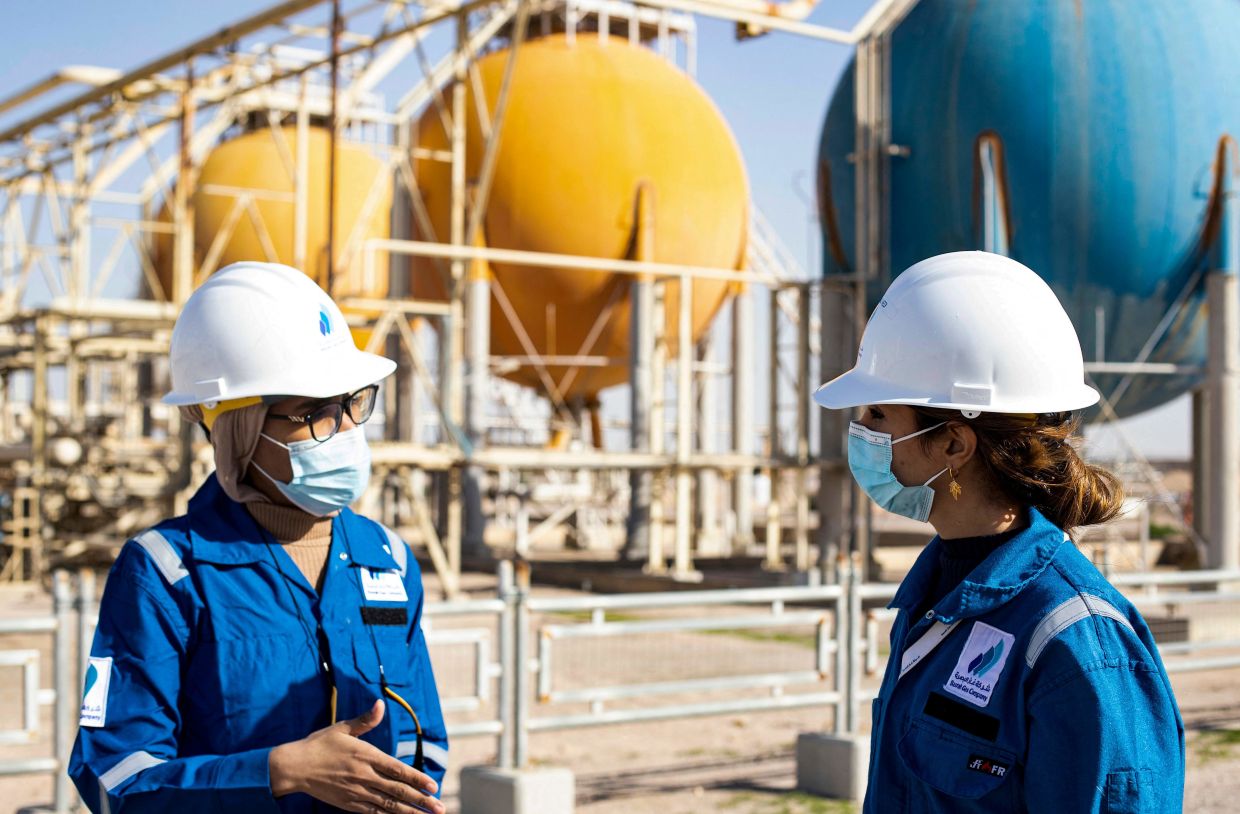 Cô Saeedi (bên phải) đang trao đổi công việc với đồng nghiệp ngay tại hiện trường với những giếng dầu khổng lồ sau lưng - Ảnh: Hussein Faleh/AFP
