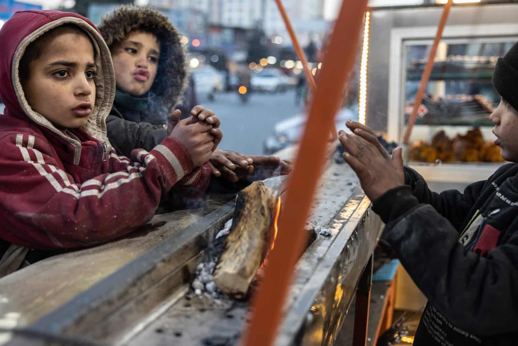 Trẻ em làm việc trên đường phố sưởi ấm bàn tay của họ bên ngọn lửa nhỏ của quầy hàng thịt nướng