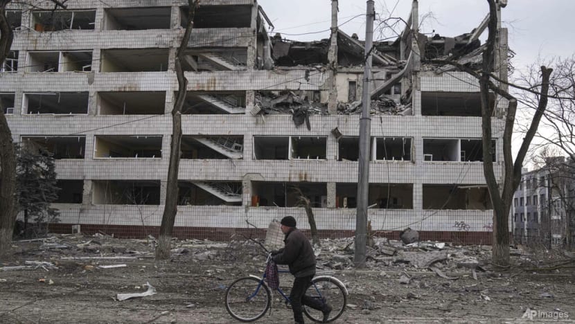 Một người đàn ông đi bộ bằng xe đạp trước một tòa nhà bị hư hại ở Mariupol, Ukraine vào ngày 10 tháng 3 năm 2022. (Ảnh: AP / Evgeniy Maloletka)