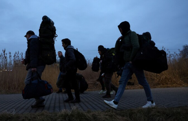 Những người đàn ông Ukraine mang theo túi của họ về phía trạm kiểm soát biên giới ở Medyka, Ba Lan, khi họ trở lại Ukraine để chiến đấu vào ngày 2 tháng 3. (Kai Pfaffenbach / Reuters)