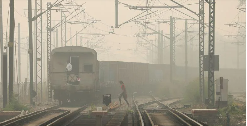 Một người phụ nữ băng qua đường ray khi một đoàn tàu chở hàng chạy qua, vào một ngày sương mù ở New Delhi
