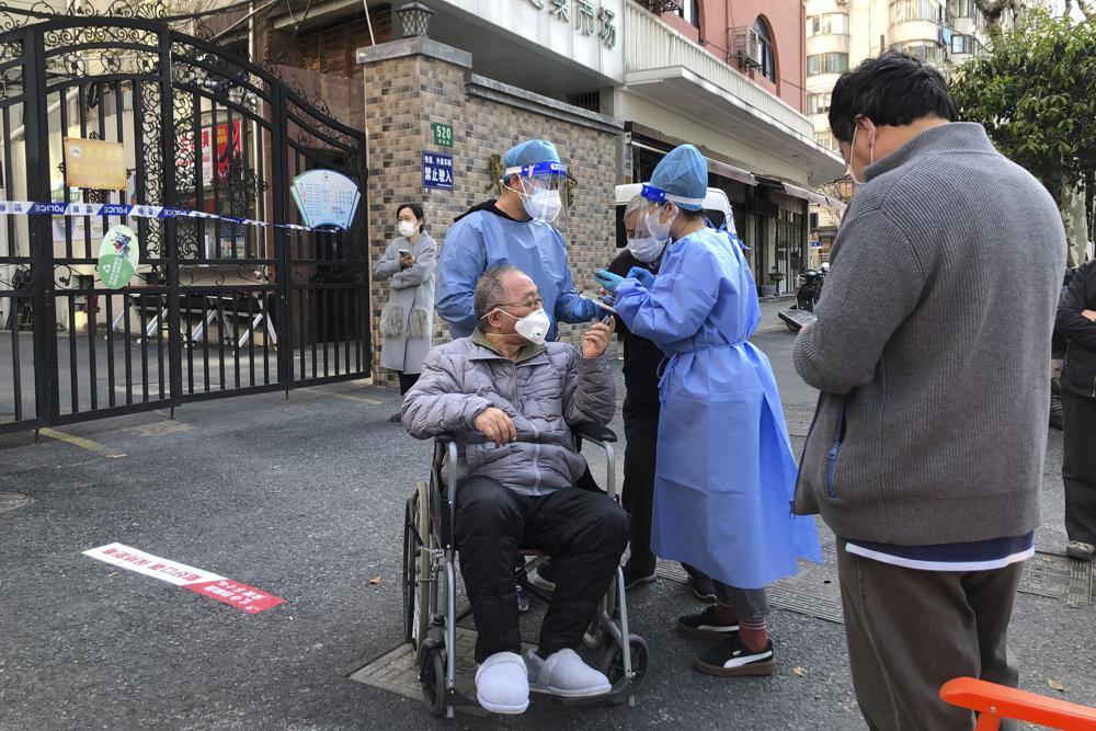 Nhân viên mặc đồ bảo hộ giúp một người đàn ông ngồi xe lăn trong cuộc xét nghiệm hàng loạt cho cư dân trong khu vực phong tỏa ở Tĩnh An, Thượng Hải