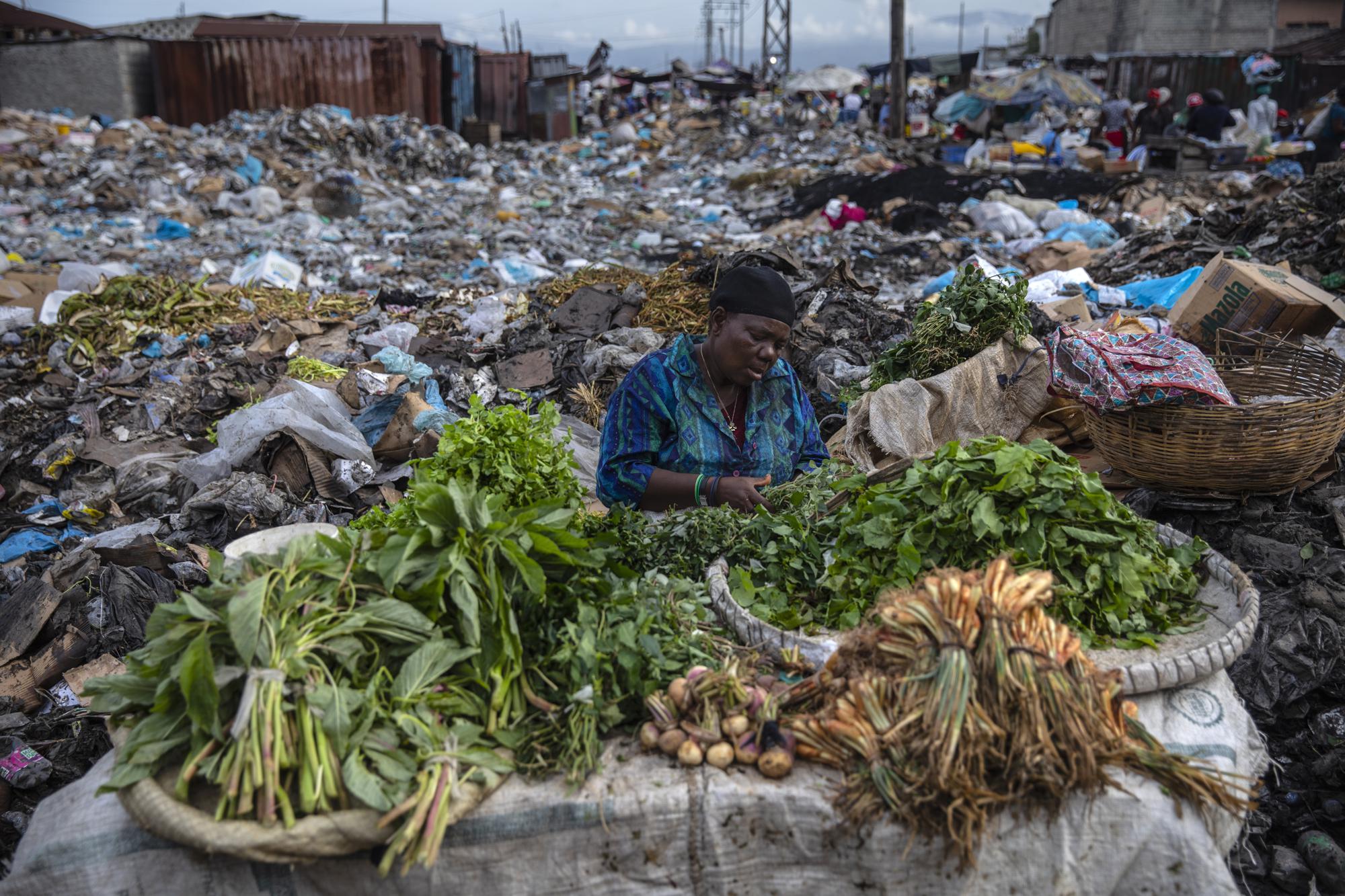 Một người phụ nữ bán rau xanh trong chợ Croix des Bosalles ở Port-au-Prince, Haiti, ngày 22/9/2021. Nền chợ dày đặc rác phân hủy, và ở một số nơi có những đám cháy nhỏ do đốt rác