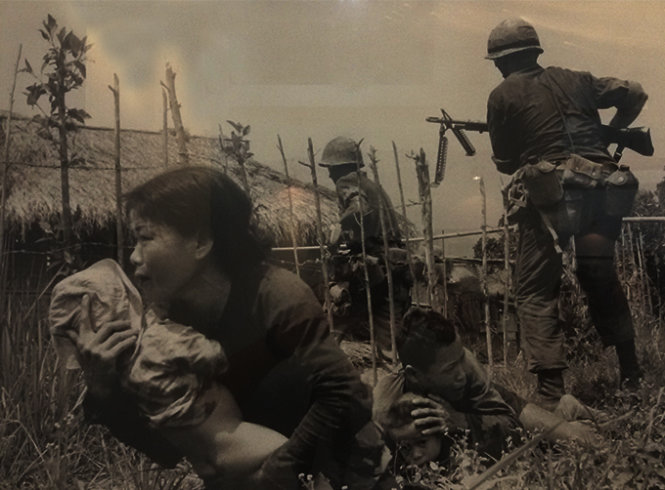 Dưới làn đạn bắn tỉa, một phụ nữ Việt Nam bế đứa trẻ đến nơi trú ẩn, trong khi lính Mỹ đang tấn công làng Mỹ Sơn, gần Đà Nẵng, để tìm quân giải phóng - Ảnh chụp lại tại triển lãm “Việt Nam - Cận cảnh cuộc chiến”.