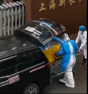 Hình ảnh cắt từ clip cho thấy người đàn ông mặc áo trắng đang cản hai nhân viên nhà xác mặc áo xanh mang túi đựng thi thể đi. Người đàn ông này đã mở túi đựng xác cho thấy bệnh nhân trong túi vẫn còn sống