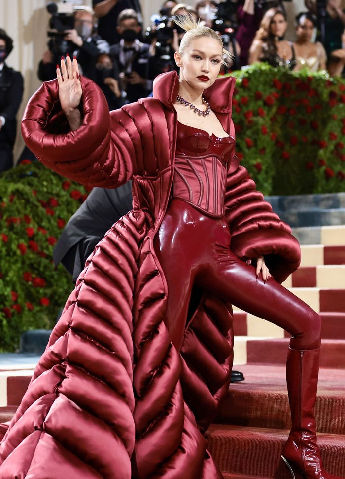 Gigi Hadid tiếp tục đốt cháy thảm đỏ với bộ áo liền quần corset màu đỏ của nhãn hiệu Versace và một chiếc áo choàng khổng lồ. Đáng chú ý bộ cánh của cô nàng được làm bằng nhựa PVC, để lộ phần xương hông quyến rũ của nữ siêu mẫu.