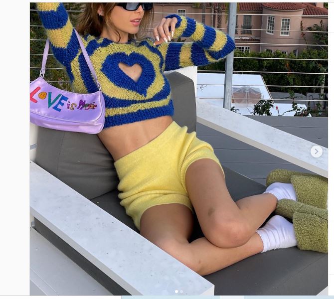 YouTuber nổi tiếng Emma Chamberlain đem đến sự kết hợp mới mẻ với áo dệt kim họa tiết cùng quần đùi và dép lê mềm. Bộ trang phúc cực kỳ thuận tiện trong việc di chuyển.