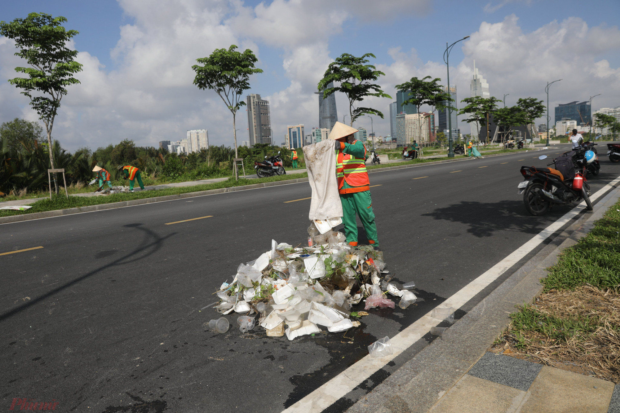 2 nữ công nhân môi trường gom các loại rác thải thành từng đống nhỏ trên đường R12 để tiện cho xe rác tới thu gom.  