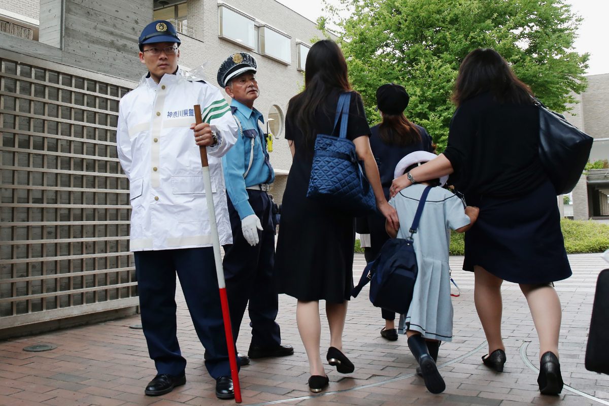 Trẻ em đến một trường tiểu học ở Kawasaki với cha mẹ của chúng không lâu sau khi một kẻ đột nhập cầm dao tấn công ở đó. Một trong những người bảo vệ mang theo một cây trượng.