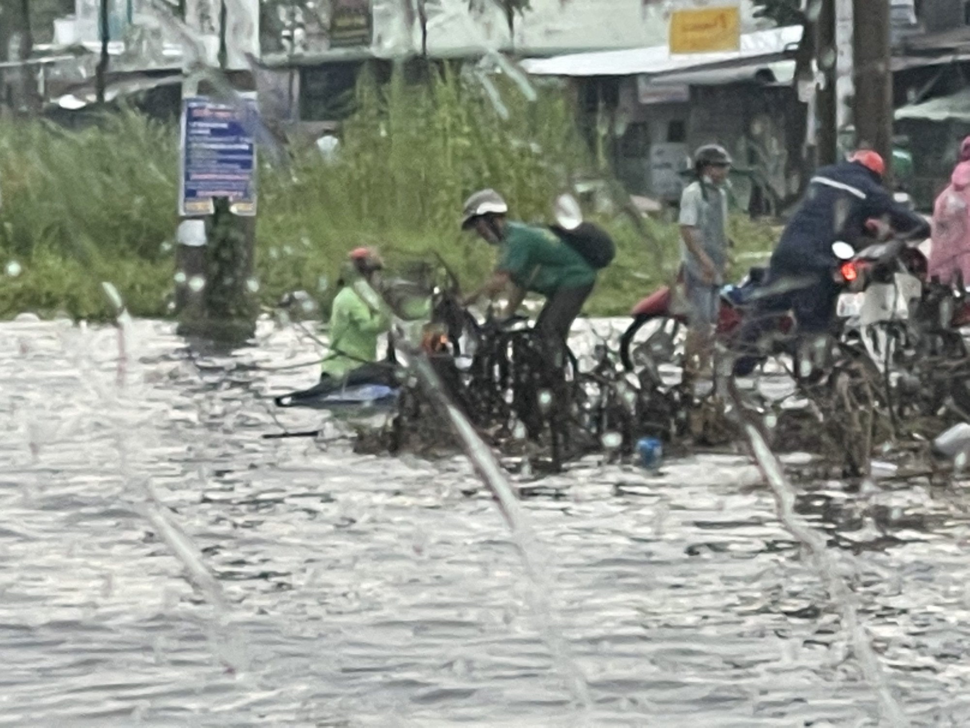 Người phụ nữ này phải chật vật mới dắt bộ được chiếc xe gắn máy ngập sâu trong nước mưa vào lề đường. Một số người dân đang hỗ trợ chị kéo chiếc xe máy lên.