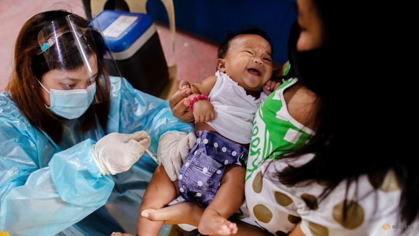 Y tá tại trung tâm y tế địa phương ở Manila, Philippinesđeo thiết bị bảo vệ cá nhân (PPE) tiêm vắc xin định kỳ cho một em bé