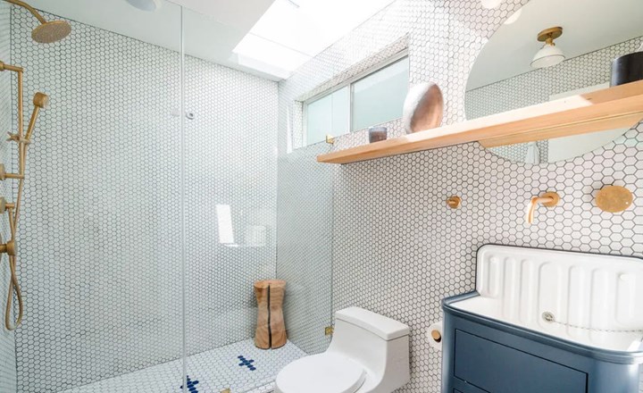 Một trong những phòng tắm của ngôi nhà, đón ánh sáng tự nhiên và lát gạch hình tròn cùng góc tắm vòi sen mở.