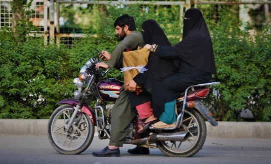 Những người phụ nữ mặc quần áo niqab che mặt ngồi trên xe máy cùng một người họ hàng trước khi đi dọc con đường ở Kabul vào tháng Năm. Ảnh: AFP