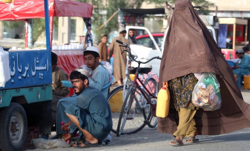 Một phụ nữ Afghanistan mặc áo khoác burqa đi ngang qua một người bán thực phẩm ven đường ở Kandahar trong tháng này. Ảnh: EPA-EFE