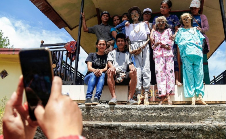 Một gia đình trên một hòn đảo của Indonesia chụp ảnh với một người họ hàng lớn tuổi không còn có thể mỉm cười, trong khi một gia tộc khác cố gắng mặc áo sơ mi và áo dài cho một trong những bậc tiền bối của họ.