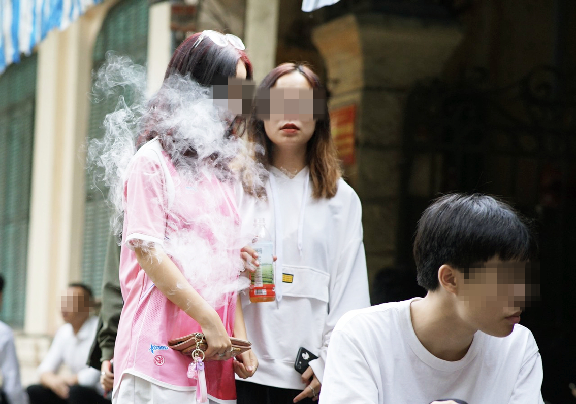 Các bạn trẻ hút thuốc lá điện tử phía trước một cổng trường thuộc phố Hai Bà Trưng (Q.Hoàn Kiếm, Hà Nội) - ẢNH: BẢO KHANG
