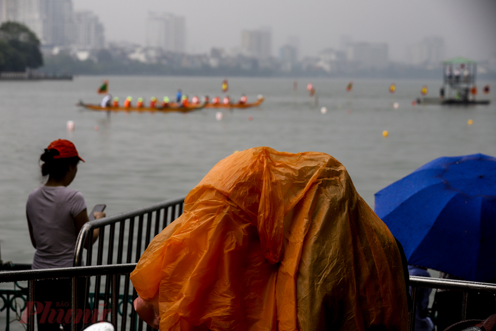 Mưa lớn, nhiều người tìm chỗ trú đứng xem, số còn lại đội mưa, mặc áo mưa để xem Bơi chải thuyền rồng.