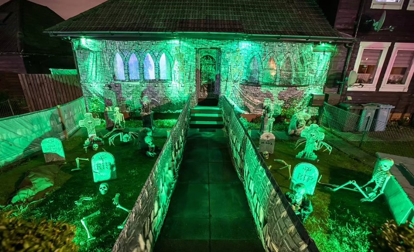 Bên ngoài ngôi nhà Halloween của ông bà Howson vào ban đêm với đèn xanh chiếu sáng nghĩa địa ma quái