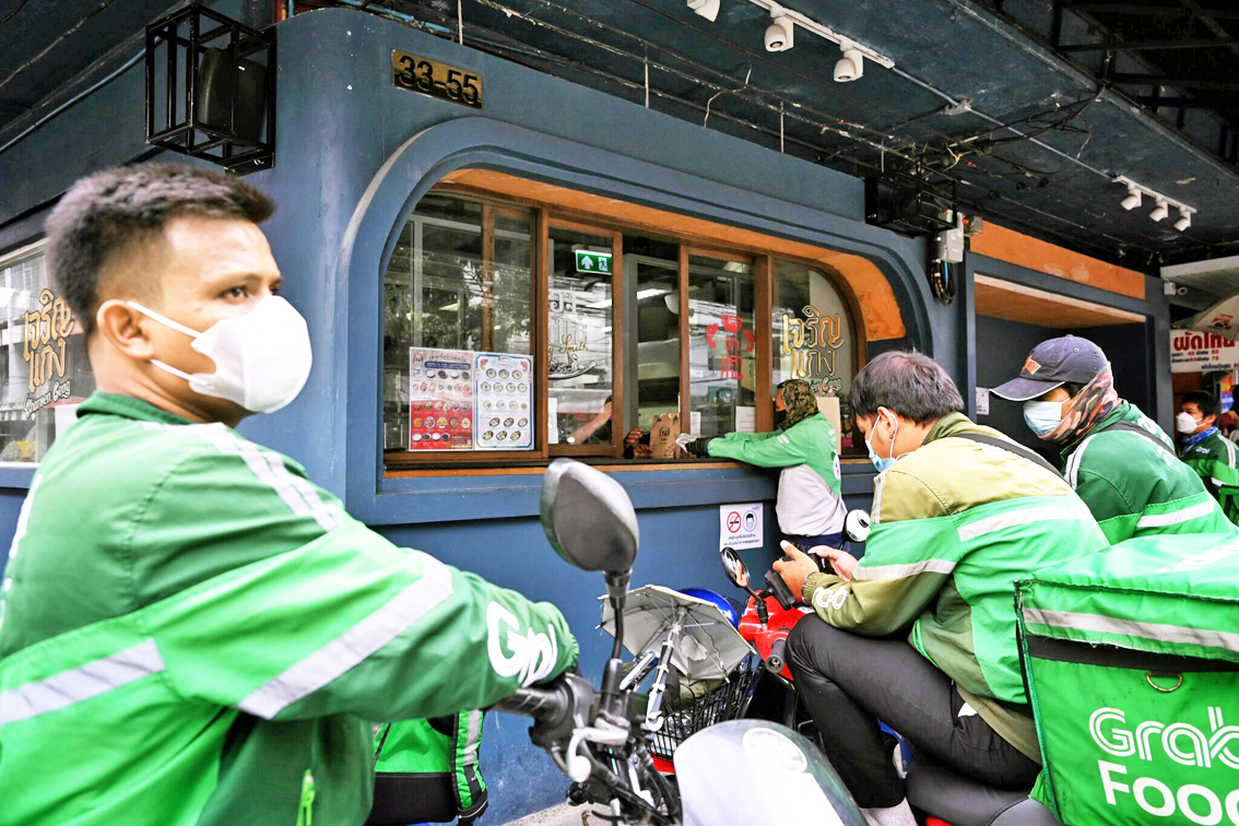 Tài xế giao hàng GrabFood chờ nhận các đơn hàng mang đi bên ngoài một nhà hàng ở Bangkok - ẢNH: AFP