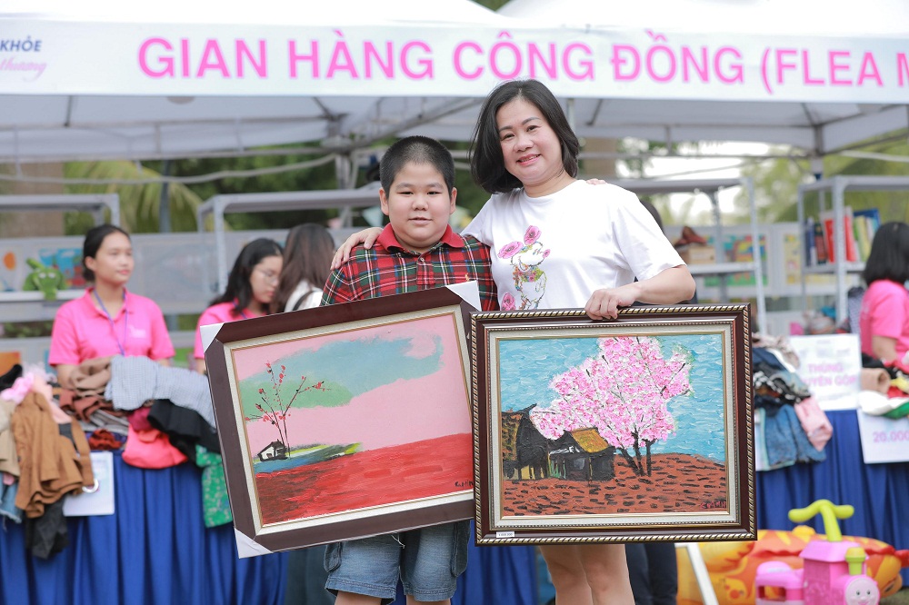 Chị Giang và bé Gia Minh tại gian cộng đồng. Riêng bức tranh “Xuân về trên bản em” (phải) của Gia Minh được bán tại sự kiện với giá 10 triệu đồng - Ảnh: TH