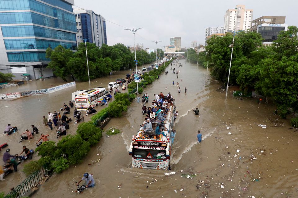 Mọi người ngồi trên nóc xe buýt trong khi những người khác lội qua con đường ngập nước trong mưa gió mùa ở Karachi, Pakistan ngày 27 tháng 8 năm 2020.