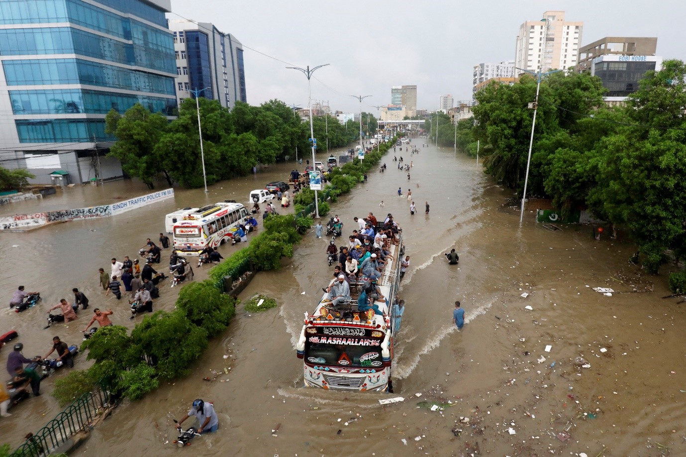 Cảnh tượng nhiều người ngồi trên nóc xe buýt trong khi những người khác đang lội qua con đường ngập nước trong bối cảnh dịch bệnh COVID-19 đang bùng phát tại Karachi, Pakistan ngày 27/8/2020. Ảnh: Reuters