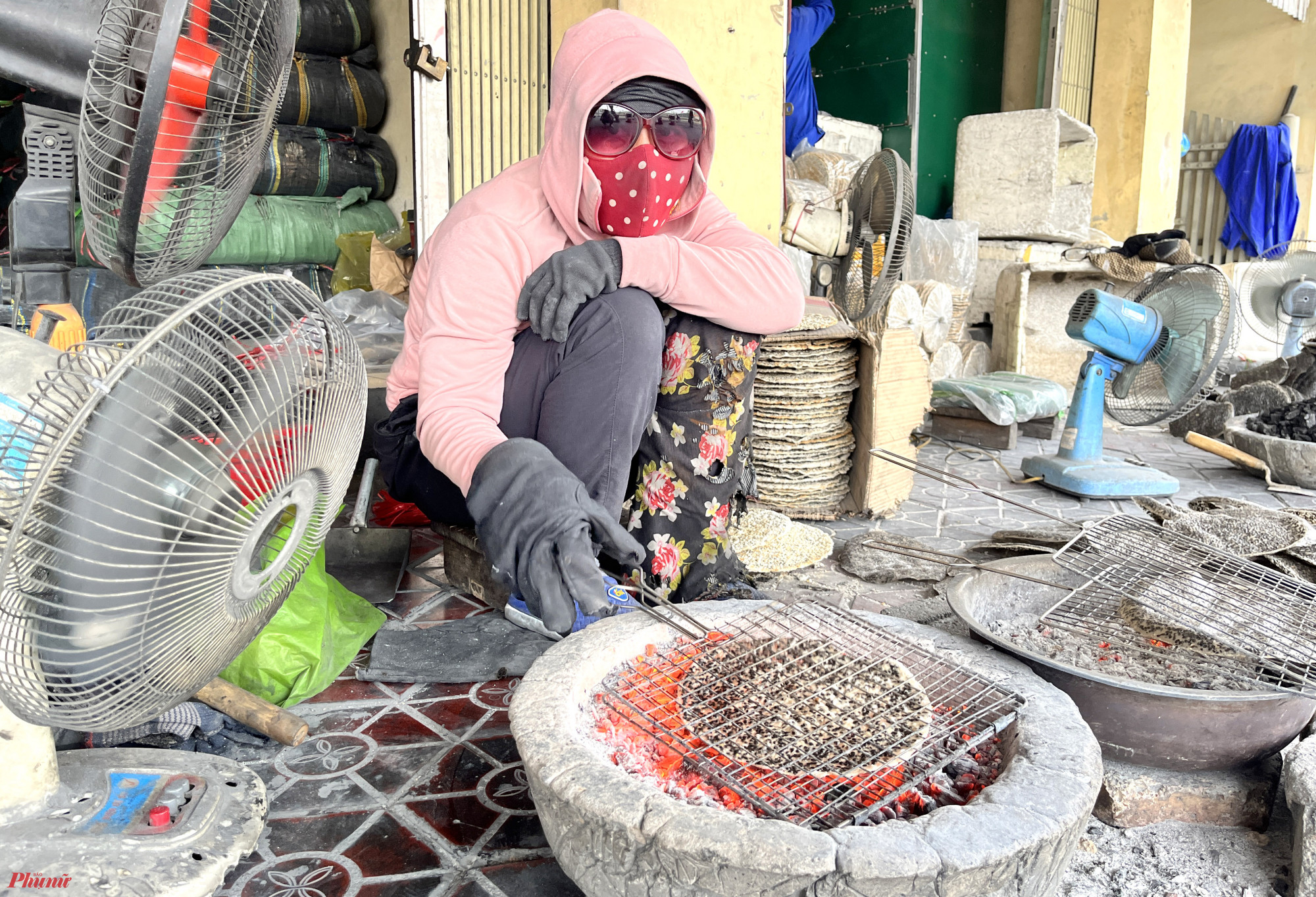 Để kịp hàng giao cho khách, hàng chục người phụ nữ phải túc trực liên tục bên những nồi than đỏ rực cả ngày để nướng bánh đa. Để nhanh hơn, mỗi người còn được bố trí thêm 2 chiếc quạt dí thẳng vào chậu than. 