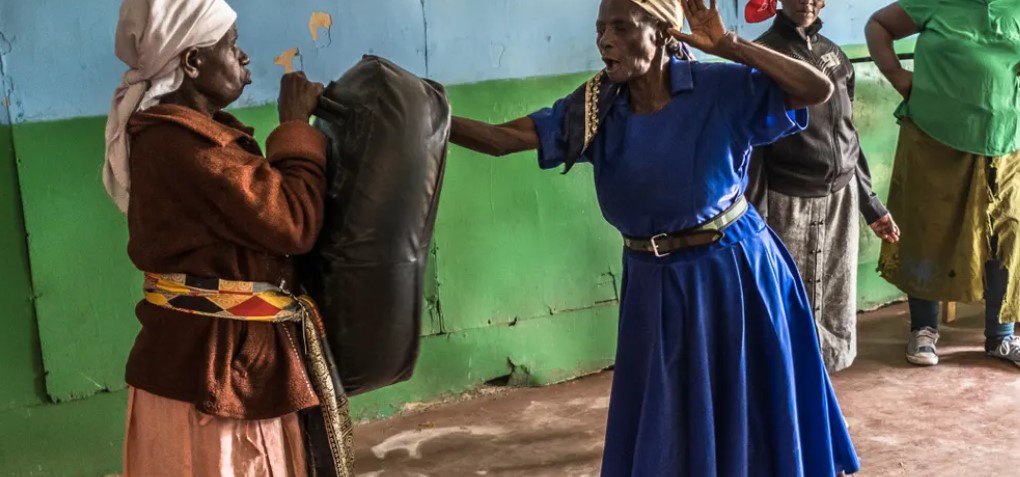 Một ngày giữa tuần, bà Beatrice Nyariara (váy xanh), 81 tuổi, đi dọc theo những con đường của khu định cư Korogocho để đến nhà thờ nhưng bà không đi lễ mà là đi đến một lớp học tự vệ. Tại khuôn viên, một nhóm phụ nữ lớn tuổi trò chuyện khi họ sắp xếp lại đồ đạc để có khoảng không tập luyện. “Đã vài tuần kể từ khi chúng tôi gặp nhau và điều quan trọng là phải bắt đầu với việc khởi động”, bà Beatrice nói khi thực hiện các động tác duỗi lưng, duỗi bên hông và chạm sàn. Những người còn lại thì thì thầm và đùa giỡn về việc cơ thể họ đang vật lộn để theo kịp Beatrice. Một người nhặt bao cát và những người còn lại xếp thành một hàng. Rồi những tiếng hét vang lên khi từng phụ nữ lần lượt đấm vào túi.