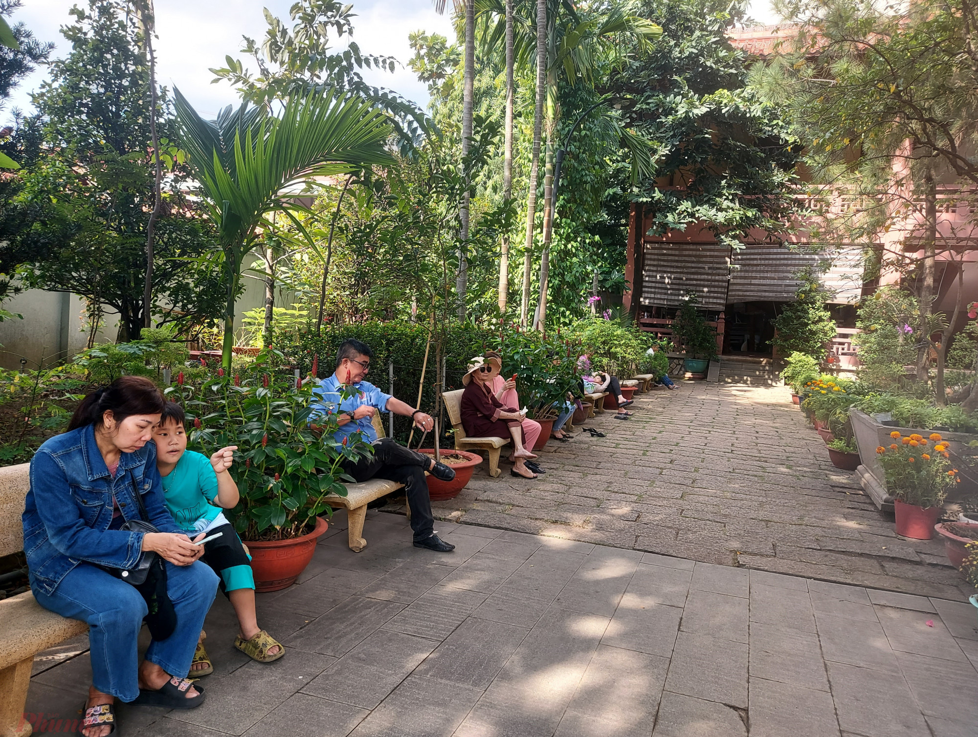 Du khách ngồi hưởng thụ không khí trong lành dưới bóng cây ở nội viện chùa Huệ Nghiêm trong ngày Rằm tháng Giêng.
