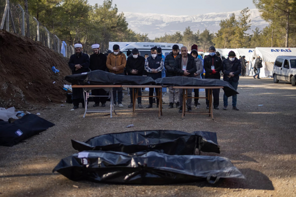 Nhóm người đưa tang cầu nguyện bên cạnh những chiếc túi đựng xác gần những ngôi mộ tập thể đang được đào ở ngoại ô Kahramanmaras