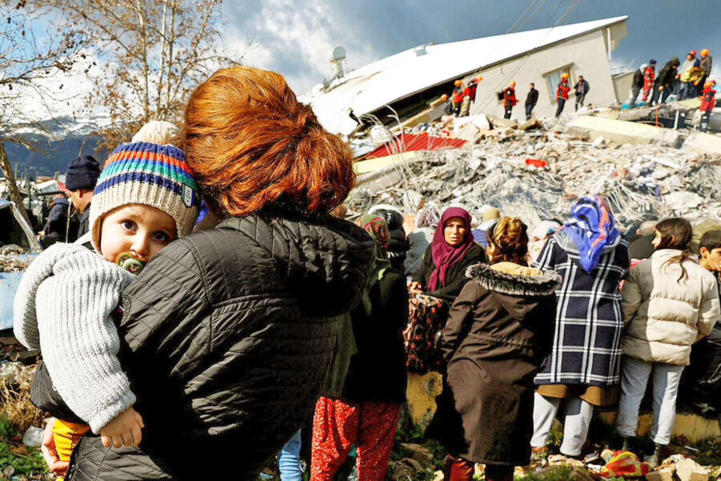 Một phụ nữ bế con đứng gần đống đổ nát sau trận động đất ở Thổ Nhĩ Kỳ - ẢNH: REUTERS