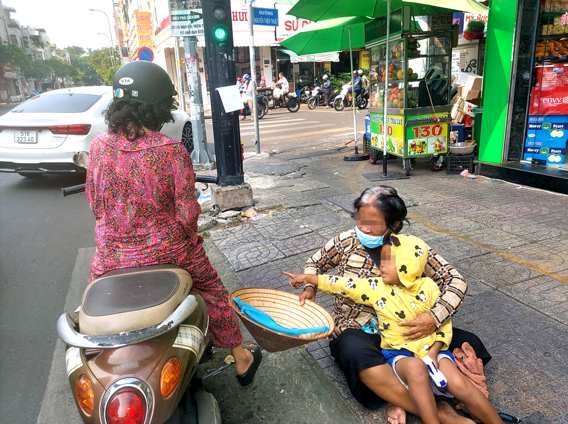 Người phụ nữ dắt theo cháu nhỏ ăn xin ở góc đường Nguyễn Đình Chiểu - Nguyễn Thiện Thuật - ẢNH: HOÀNG LÂM