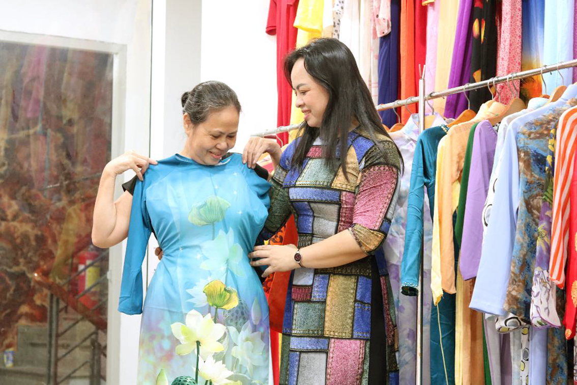 Chị Bích (bìa trái) xúc động khi được chị Đoàn Thị Nguyệt - chủ nhà may Hải Triều - tặng bộ áo dài mới 
