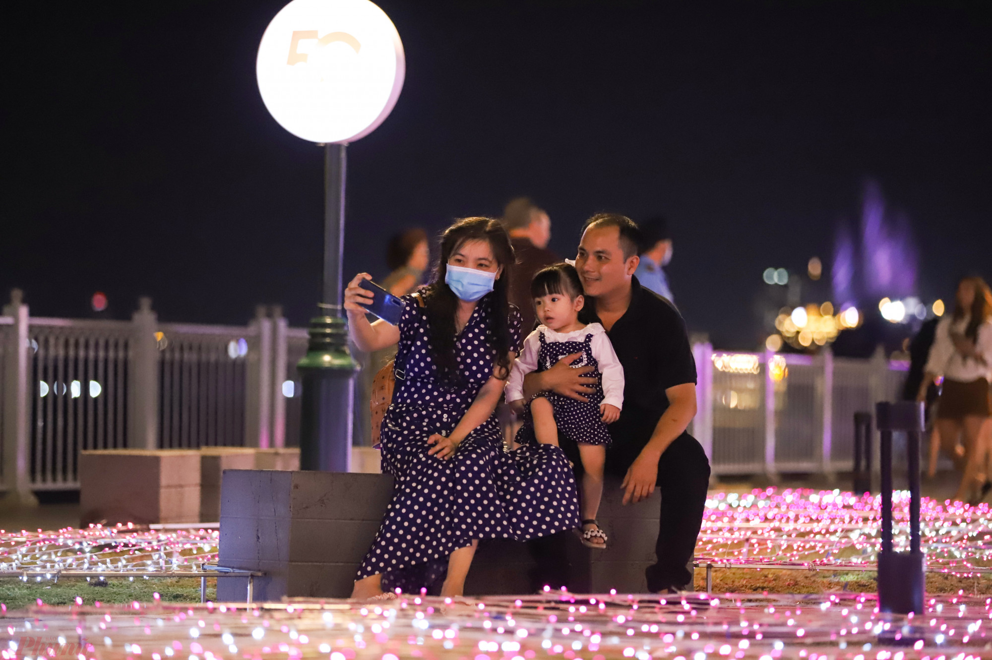 Gia đình chị Nhung (quận 7) chụp hình check-in bên dàn đèn LED được lắp đặt trải đều ở thảm cỏ công viên.