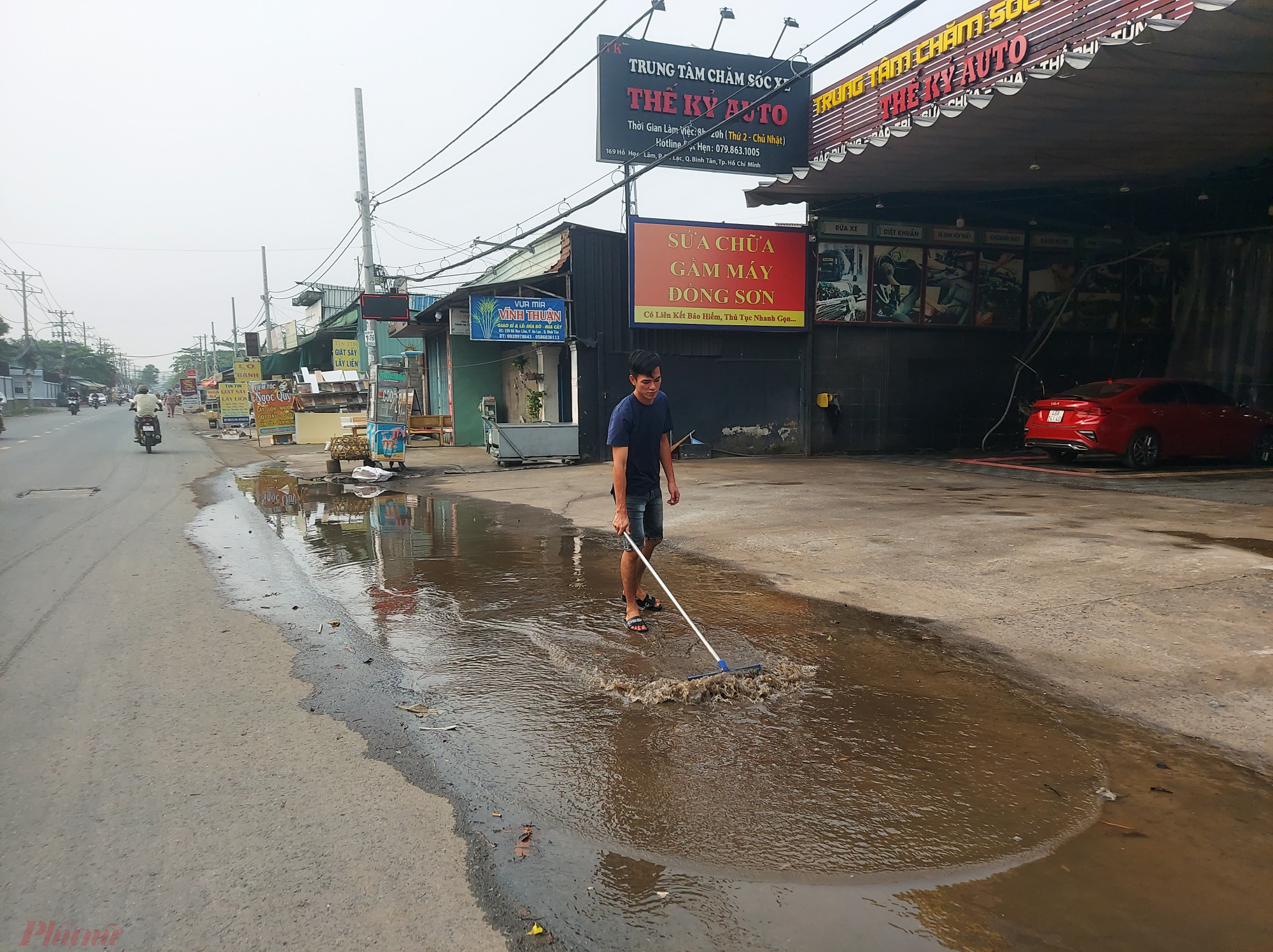 Nhân viên một cửa hàng sửa ô tô trên đường Hồ Học Lãm xử lý nước đọng trước cửa hàng sau trận mưa đêm qua.