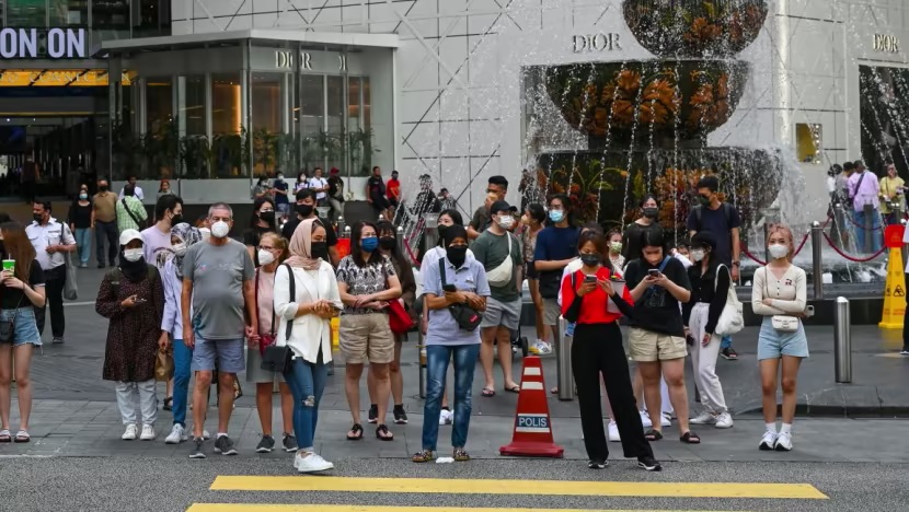 Người dân đeo khẩu trang đứng chờ băng qua đường trước một trung tâm mua sắm ở Kuala Lumpur