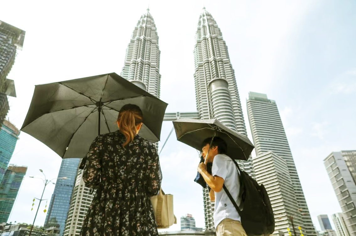 Một cặp đôi dùng dù che nắng khi đi dạo ở Kuala Lumpur vào tháng Tư - ẢNH: EPA-EFE