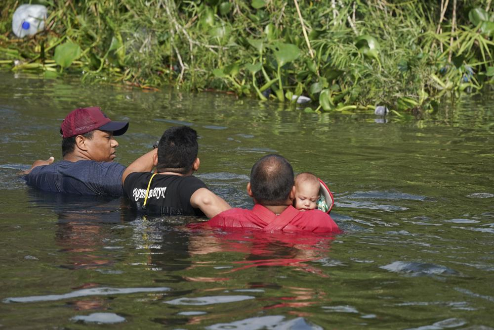 Một người di cư băng qua sông Rio Grande với em bé trong tay, nhìn từ Matamoros, Mexico, hôm 10/5. (Ảnh: AP)