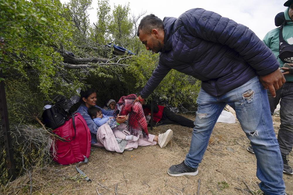 Một người di cư từ Colombia (phải) đưa mền cho một phụ nữ đồng hương có con nhỏ khi cả nhóm chờ xin tị nạn sau khi vượt biên. (Ảnh: AP)