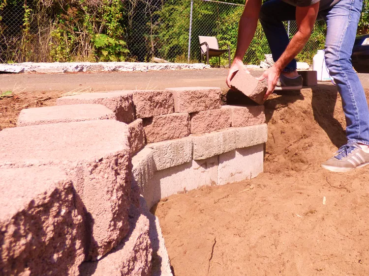 Gia cố bằng các khối tường chắn Khi bạn đến gần các cạnh của ao, hãy củng cố chu vi của tầng cuối cùng bằng các khối tường chắn  đặt trên các khối bê tông. Điều này đặc biệt quan trọng nếu địa điểm xây dựng có đất cát, tơi xốp—những khối này sẽ giúp duy trì hình dạng và chiều cao của ao. Hãy nhớ rằng các khối tường chắn nhỏ giúp bạn linh hoạt hơn và dễ thi công hơn.