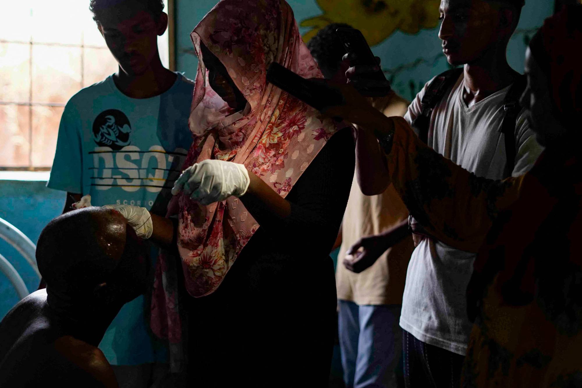 Mọi người sử dụng đèn pin trên điện thoại của họ để hỗ trợ một người phụ nữ khâu đầu cho một người đàn ông ở thành phố song sinh Omdourman của Khartoum hôm thứ Ba. | AFP-JIJI