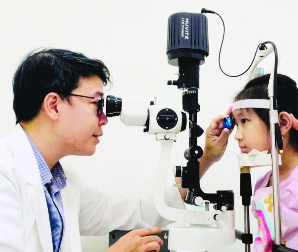 Bác sĩ Trần Đình Minh Huy đang khám tầm soát tật khúc xạ cho trẻ - ảnh: N.L.