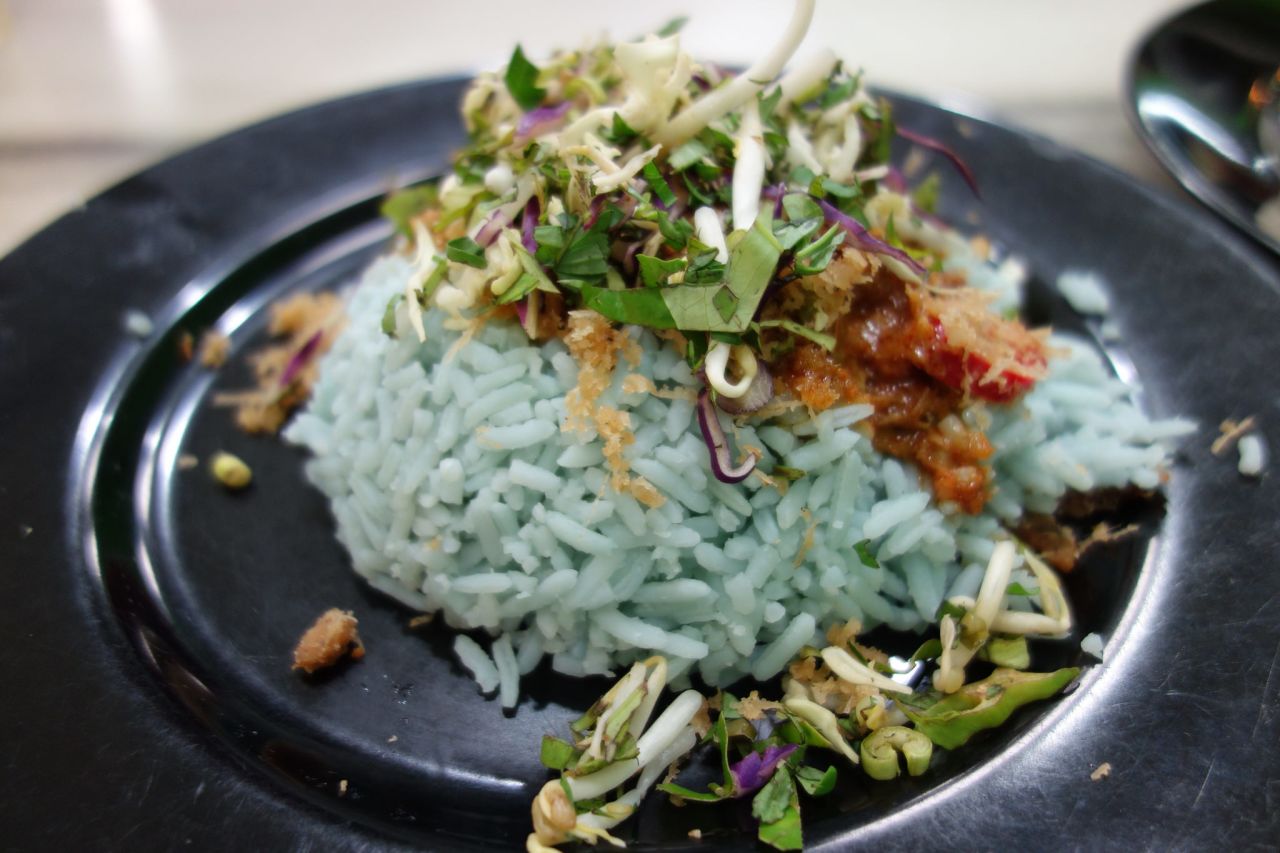 Được dịch từ tiếng Anh-Nasi kerabu là một món cơm của Malaysia, một loại nasi ulam, trong đó cơm có màu xanh lam được ăn với cá khô hoặc gà rán, bánh quy giòn, dưa chua và các loại salad khác. Màu xanh của gạo đến từ những cánh hoa Clitoria ternatea, được sử dụng làm màu thực phẩm tự nhiên khi nấu.