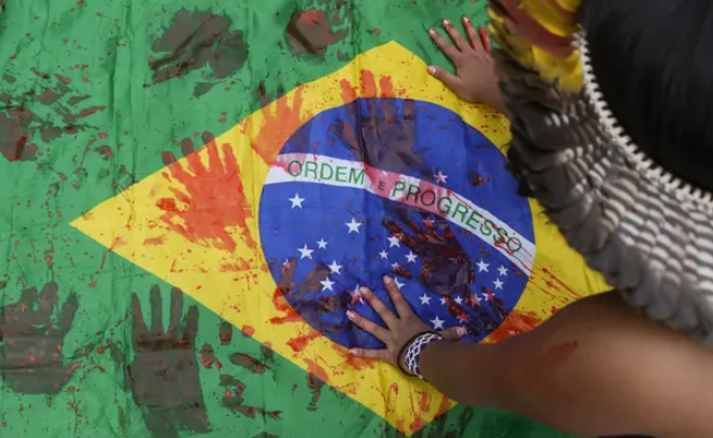 Một cô gái thổ dân in dấu bàn tay bằng sơn đỏ, tượng trưng cho máu, lên quốc kỳ Brazil. Ảnh: André Penner/AP