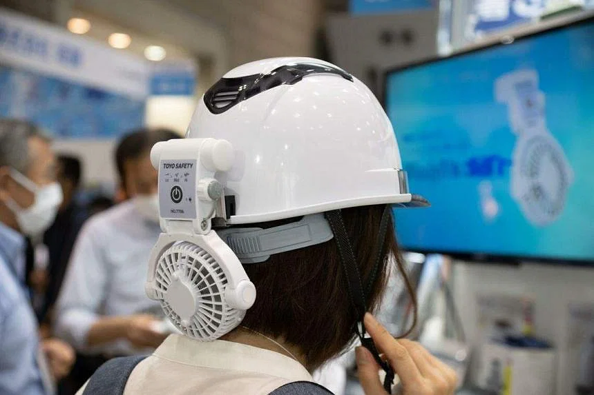 Một du khách đội mũ bảo hiểm của Công ty Toyo Safety với một chiếc quạt tại Triển lãm Giải pháp Nhiệt ở Tokyo