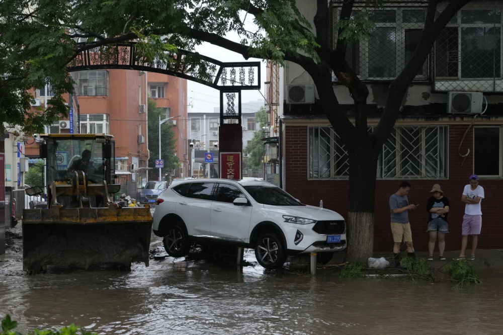 Một chiếc máy ủi được sử dụng để đẩy bùn ra khỏi một khu phố, cạnh đó là một chiếc xe bị mắc kẹt do nước lũ ở quận Mentougou, ngày 1/8 - Ảnh: AP