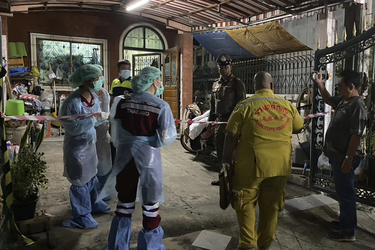 Các nhân viên pháp y Thái Lan và một nhân viên cứu hộ đến ngôi nhà nơi một người phụ nữ và hai con trai của bà thiệt mạng và người chồng được phát hiện bị thương nặng. Ảnh: AP