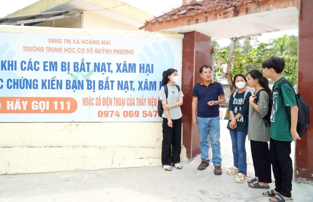Thầy Hồ Anh Tuấn (thứ hai từ trái sang) bên cạnh tấm bảng  ghi số điện thoại của hiệu trưởng để học sinh phản ánh vụ việc  bạo lực học đường - ẢNH: HÀ VINH